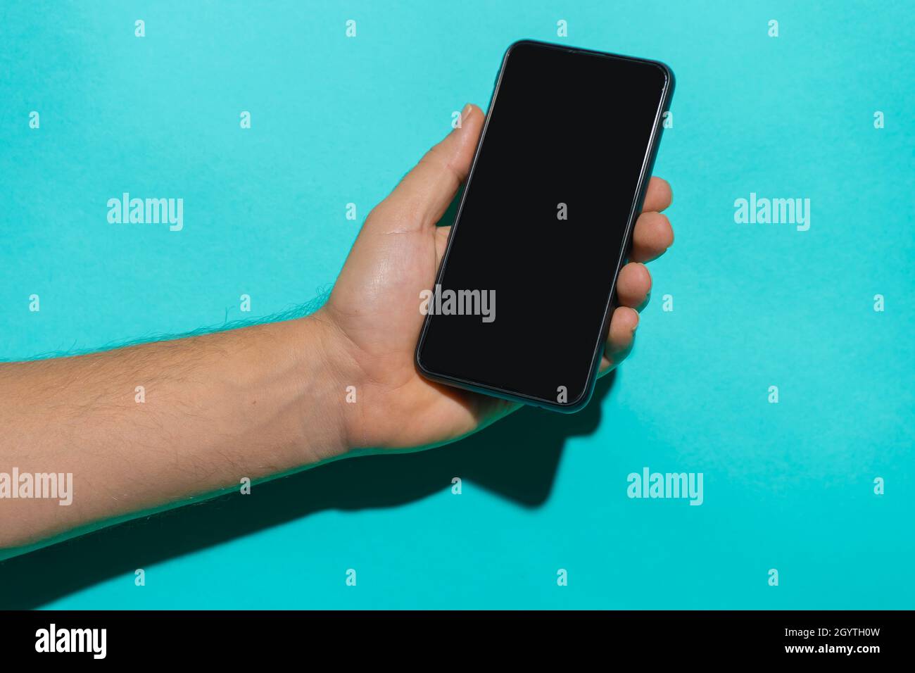 Smartphone mockup con mano uomo che tiene il telefono di fronte a uno sfondo blu colorato con spazio di copia per il testo. Foto Stock
