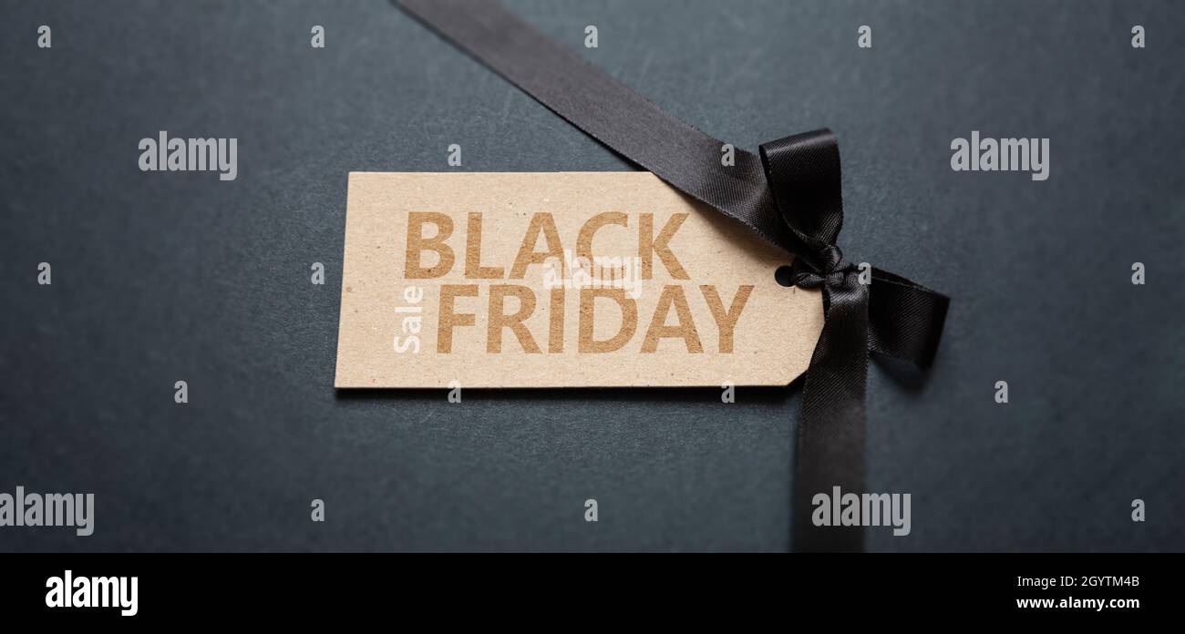 Black Friday Vendita testo scritta su un prezzo tag, sfondo scuro. Offerte speciali stagionali segno, carta kraft marrone e fiocco nastro satinato, banner Foto Stock