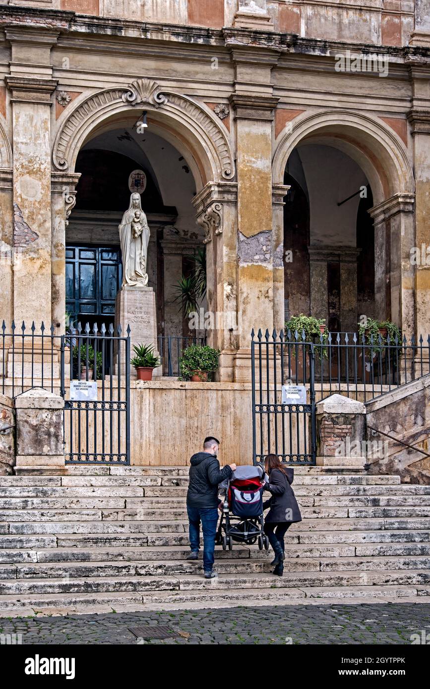 La giovane coppia porta un buggy per bambini sui gradini della Chiesa di Sant'Eusebio verso una statua della Vergine Maria che tiene il bambino Gesù. Roma, Italia. Foto Stock