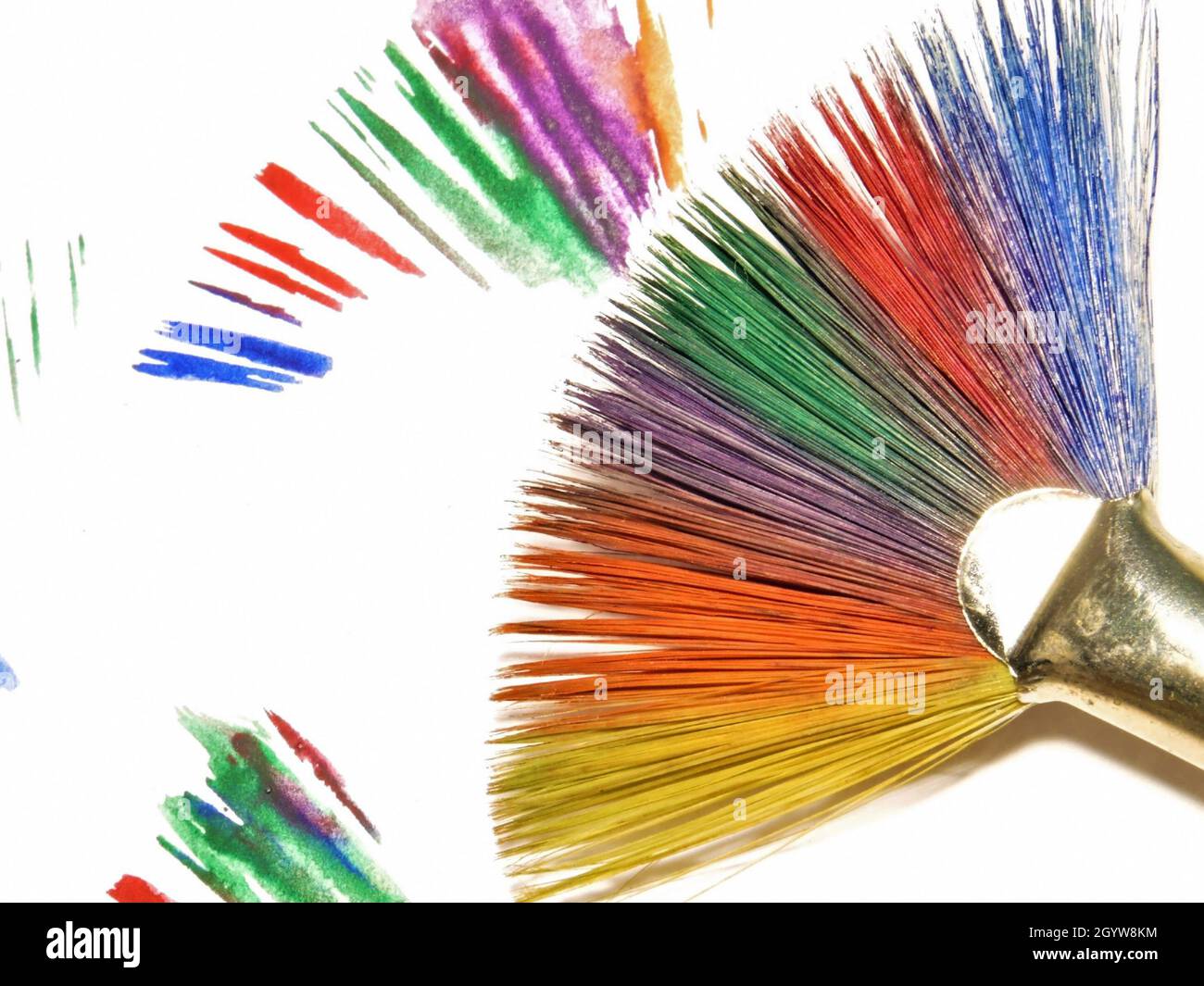 Primo piano di un pennello dipinto in colori arcobaleno su uno sfondo bianco con pennellate colorate. Foto Stock