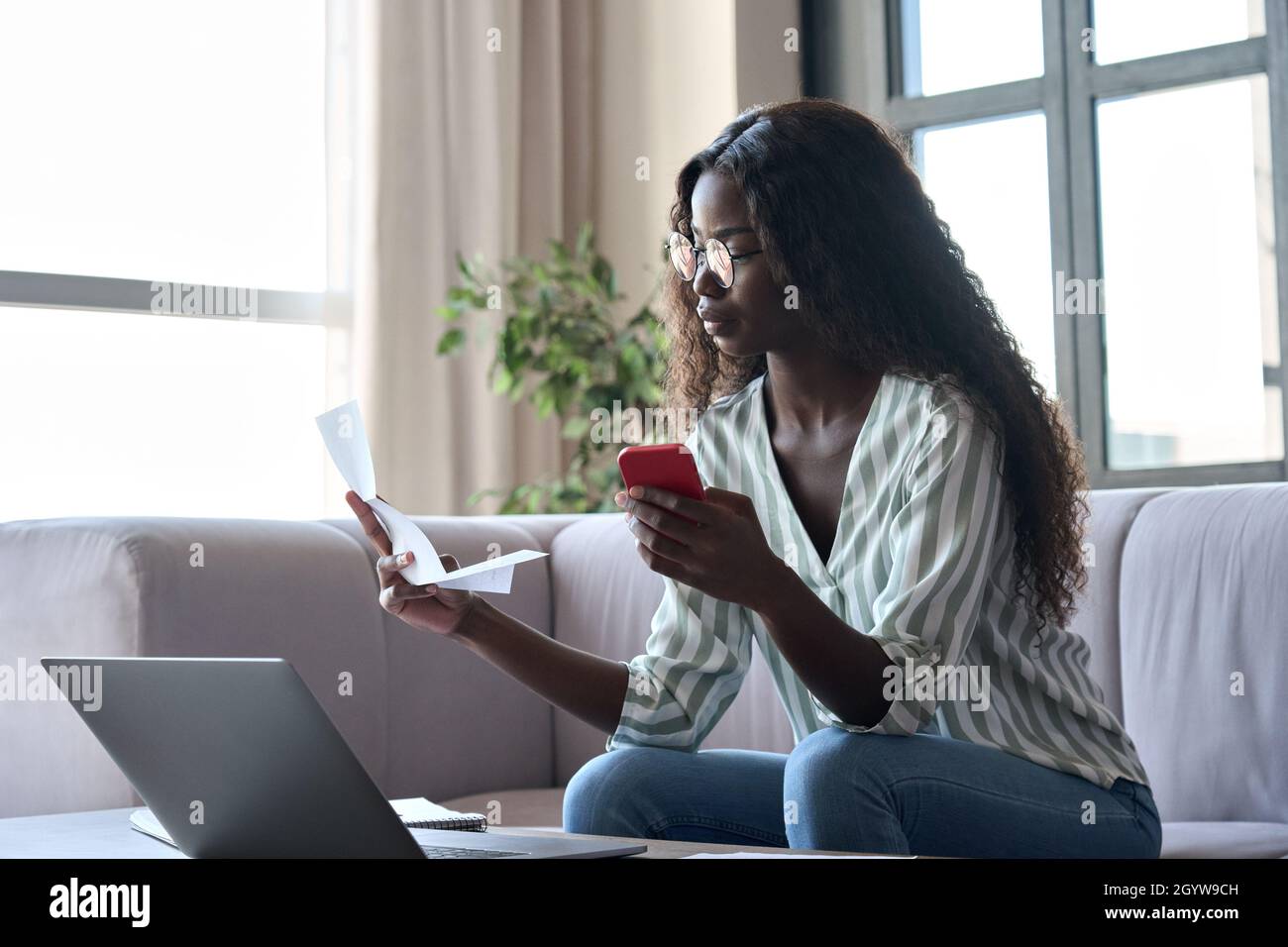 Giovane donna nera in possesso di carta che paga le fatture in applicazione mobile sul cellulare. Foto Stock