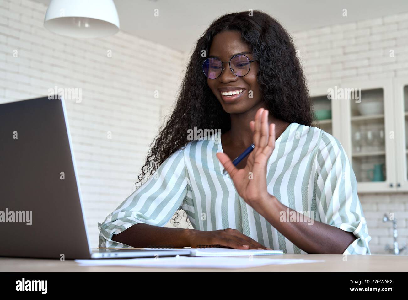 Felice donna nera che sventolano con una videochiamata virtuale guardando il notebook a casa. Foto Stock