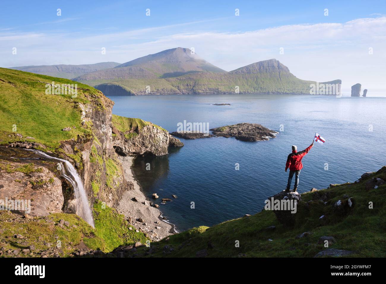 Turista vicino alla cascata di Skardsafossur sull'isola di Vagar, Isole Faroe. La vista del mare di Drangarnir Stori Drangur e il più piccolo è Lilli Foto Stock