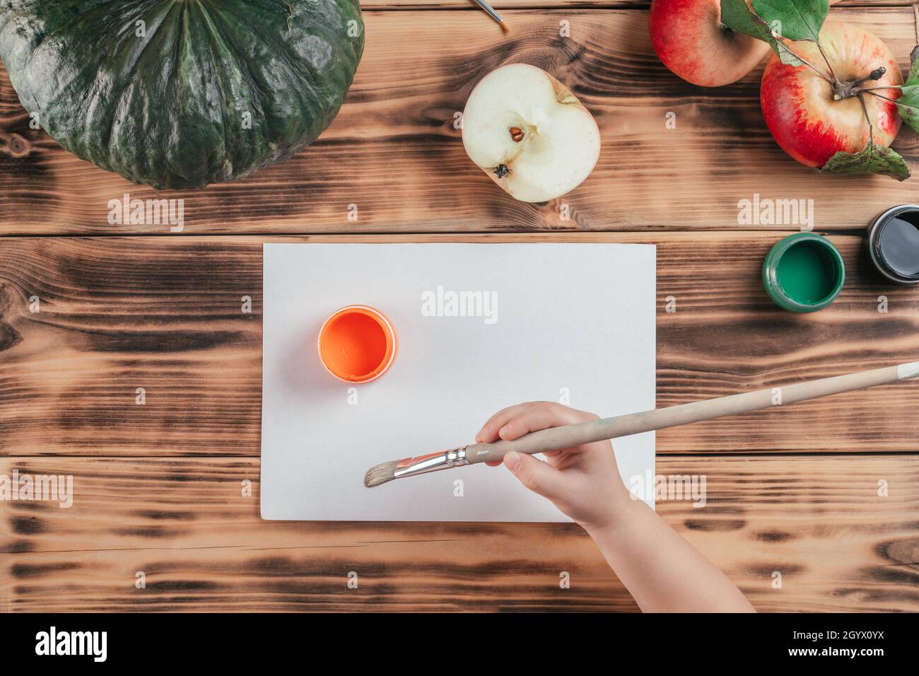 Passo-per-passo Halloween bambini tutorial stampe di mela zucca. Passo 4: La mano del bambino tiene il pennello vicino alla vernice arancione del gouache. Vista dall'alto Foto Stock