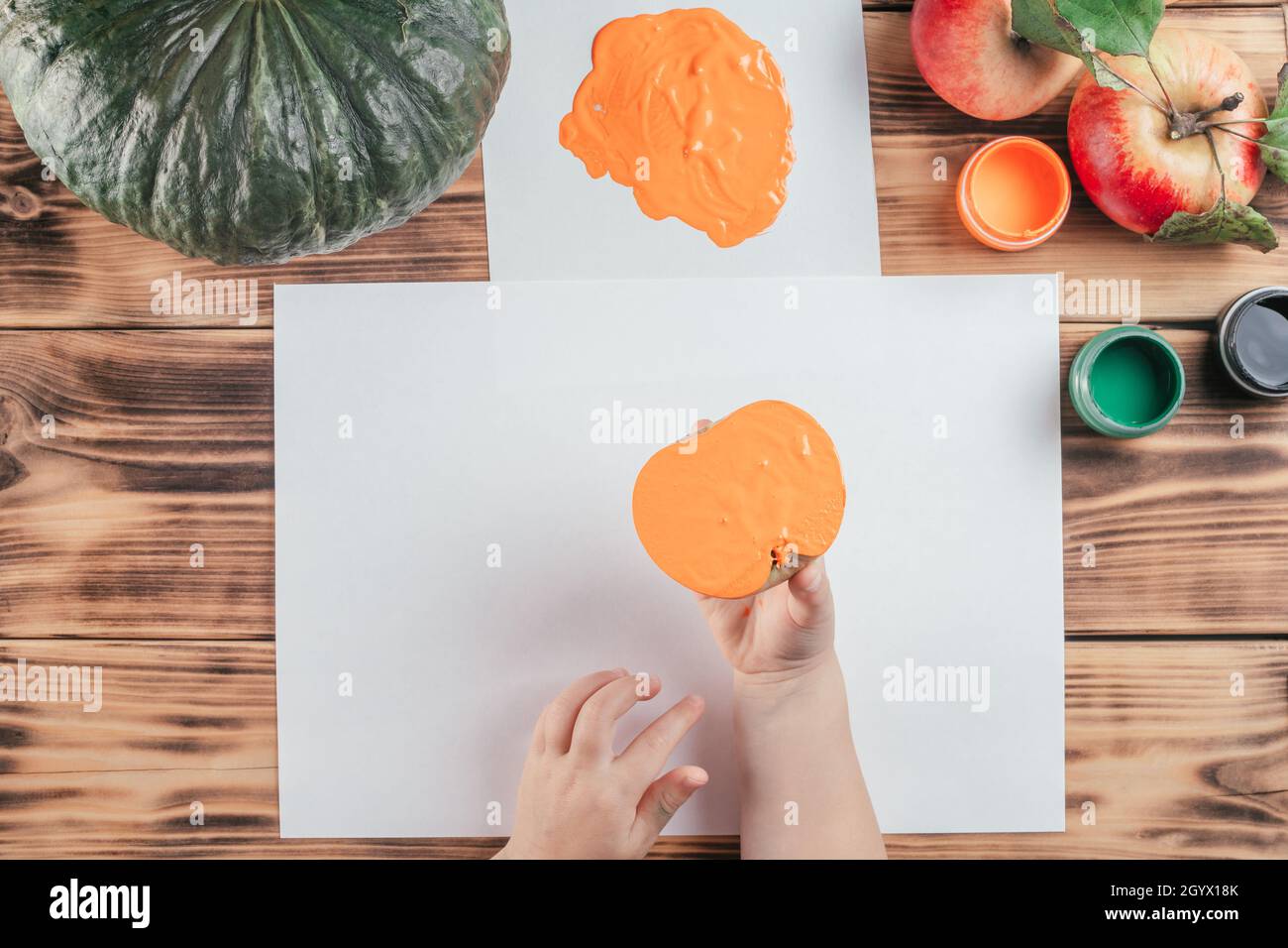 Passo-per-passo Halloween bambini tutorial stampe di mela zucca. Passo 7: La mano del bambino tiene metà della mela dipinta in gouache arancione per fare la stampa. Top vi Foto Stock