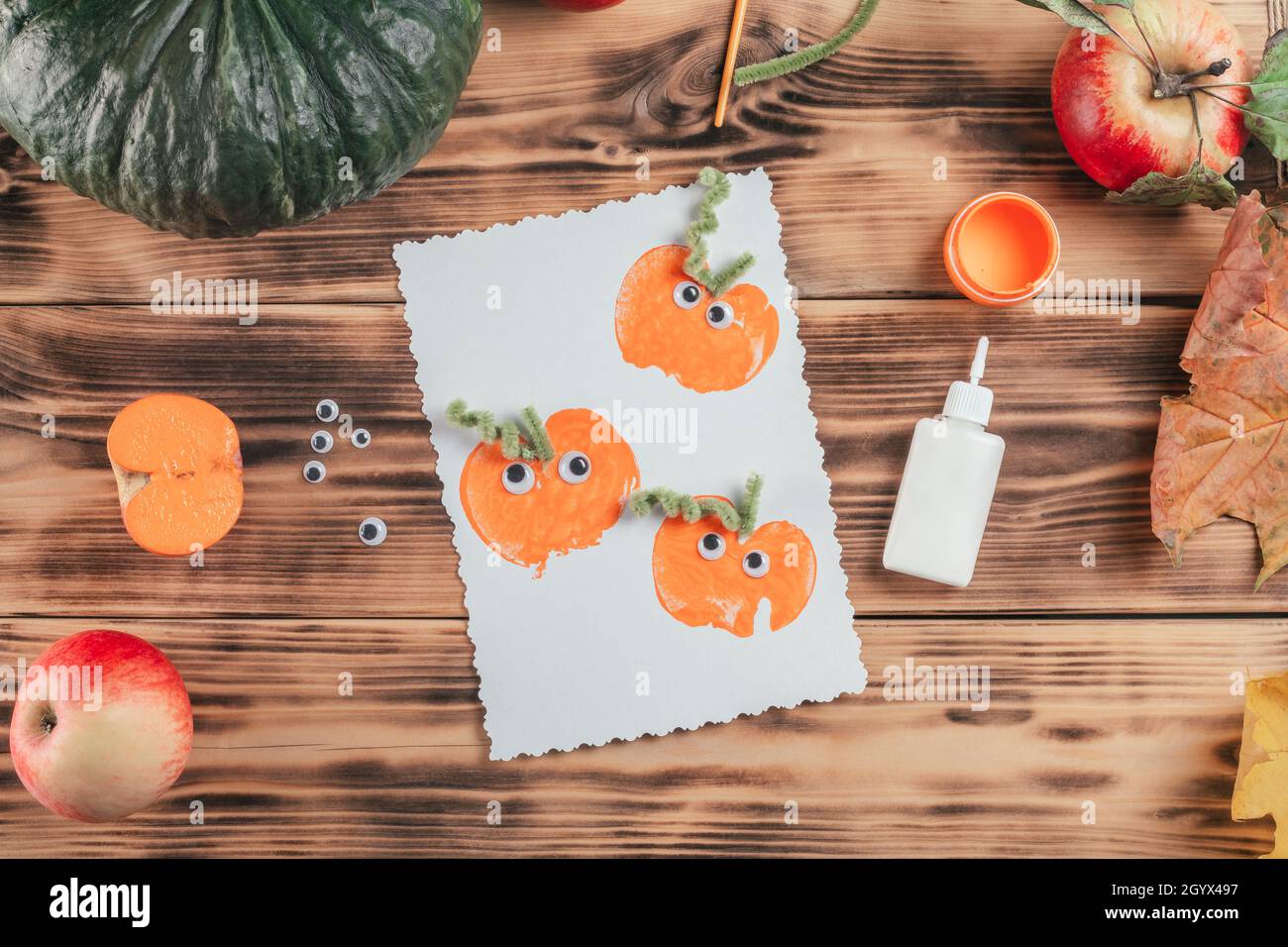 Carta di Halloween finita fatta con le stampe di mela di zucca si trova accanto a colla e vernice su superficie di legno. Vista dall'alto Foto Stock