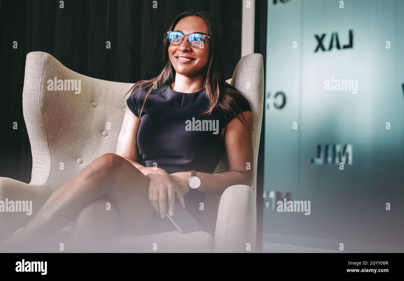 Felice giovane donna d'affari sorridente nel suo ufficio. Giovane donna d'affari seduta su una sedia e con uno smartphone in un ambiente di lavoro moderno. Sicuro voi Foto Stock