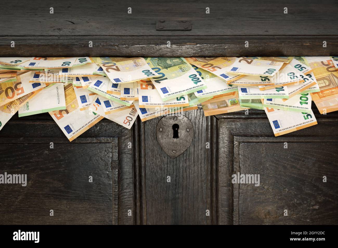 Antico petto di legno da cui fuoriescono bollette in euro. Risparmio, denaro nero, contanti, flusso di cassa. Foto Stock