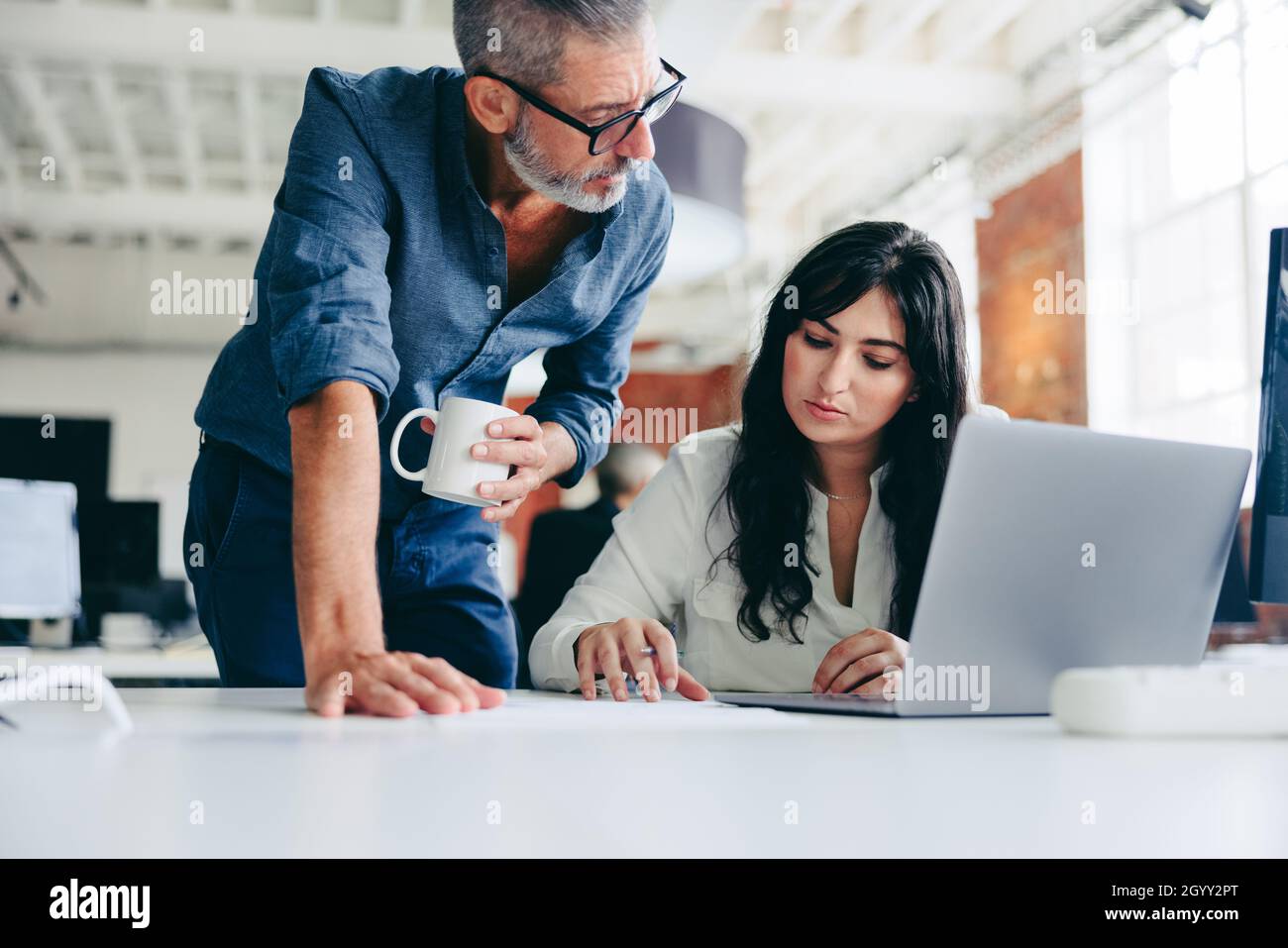 Collaborare all'ultimo progetto. Un uomo d'affari maturo e concentrato che lavora in squadra con la sua collega in un ufficio moderno. Due colleghi hanno un disGU Foto Stock