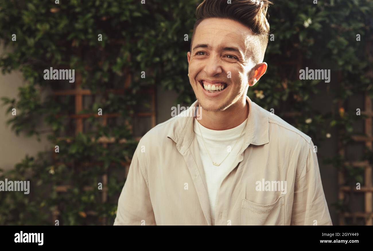 Felice transman sorridente all'aperto. Giovane uomo transgender che guarda allegro mentre in piedi da solo durante il giorno. Uomo giovane e sicuro di sesso non conforme Foto Stock