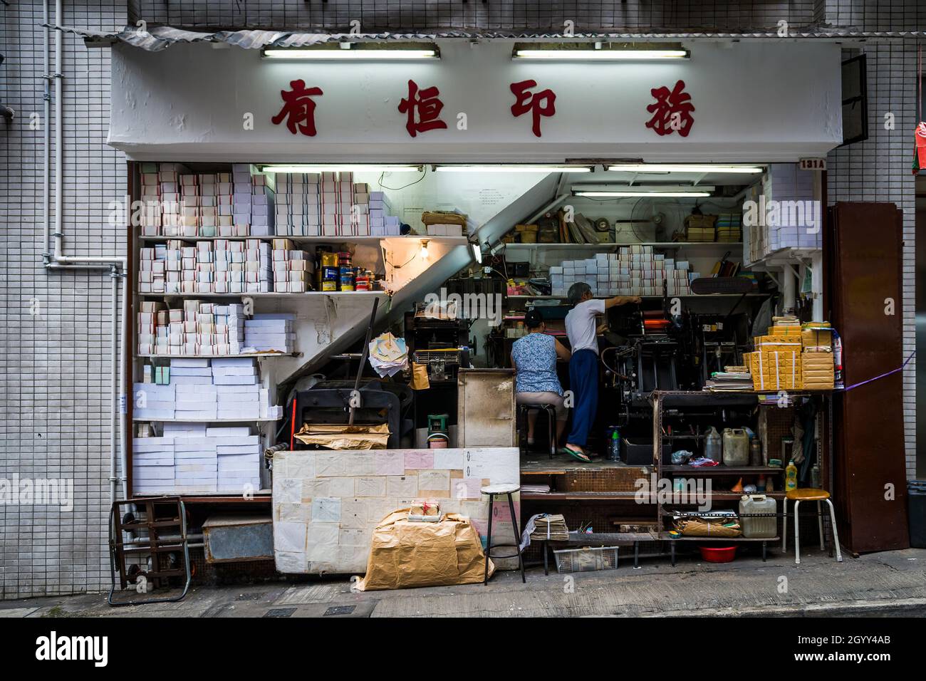 Una coppia cinese opera un'attività di stampa dallo spazio sotto una scala in Wellington Street, Central, Hong Kong Island Foto Stock