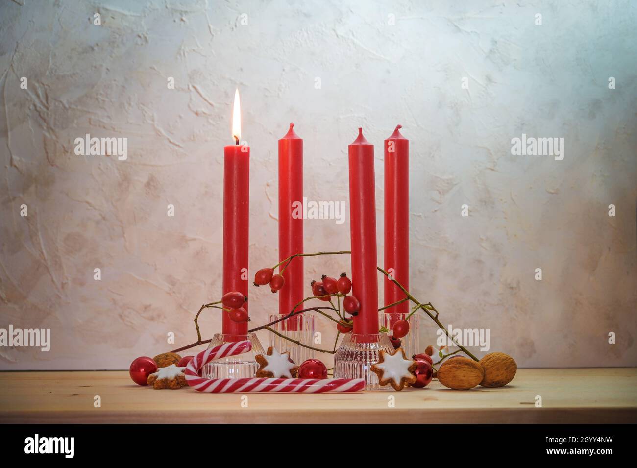 Quattro candele rosse, una si accende per la prima Domenica prima di Natale, decorazione dell'Avvento su un tavolo di legno contro una parete rustica, spazio copia, selezionato fo Foto Stock