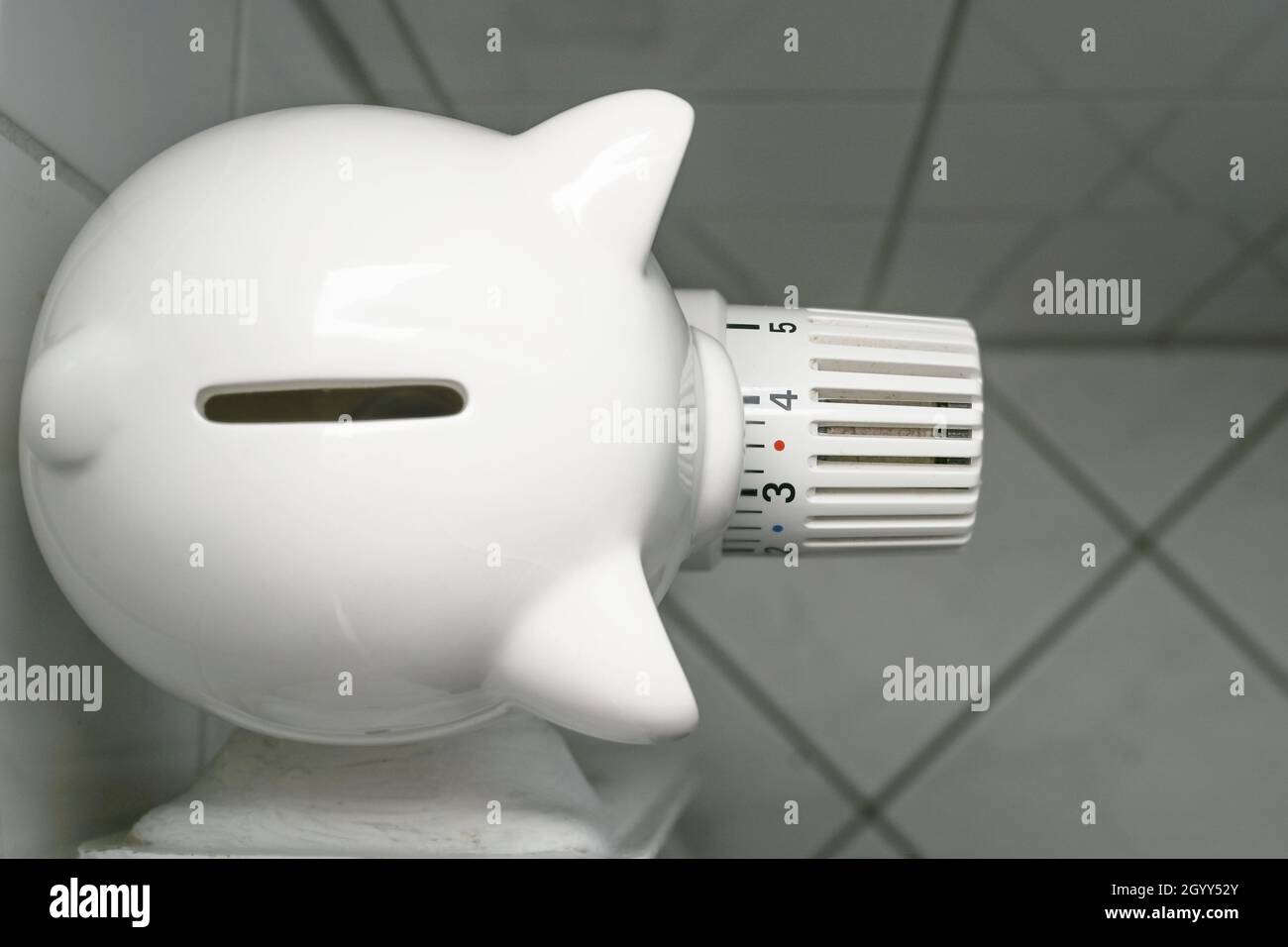 Piggy banca dall'alto sul termostato di un vecchio radiatore, concetto per aumentare i costi di calore ed energia, prospettiva divertente, fuoco selezionato, stretto Foto Stock
