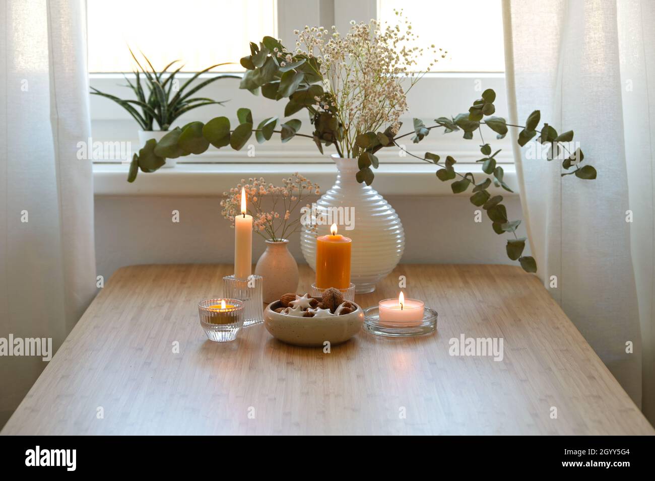 Quattro diverse candele dorate, vaso con rami di eucalipto e una ciotola con biscotti, decorazione festiva per l'Avvento e Natale su un legno Foto Stock