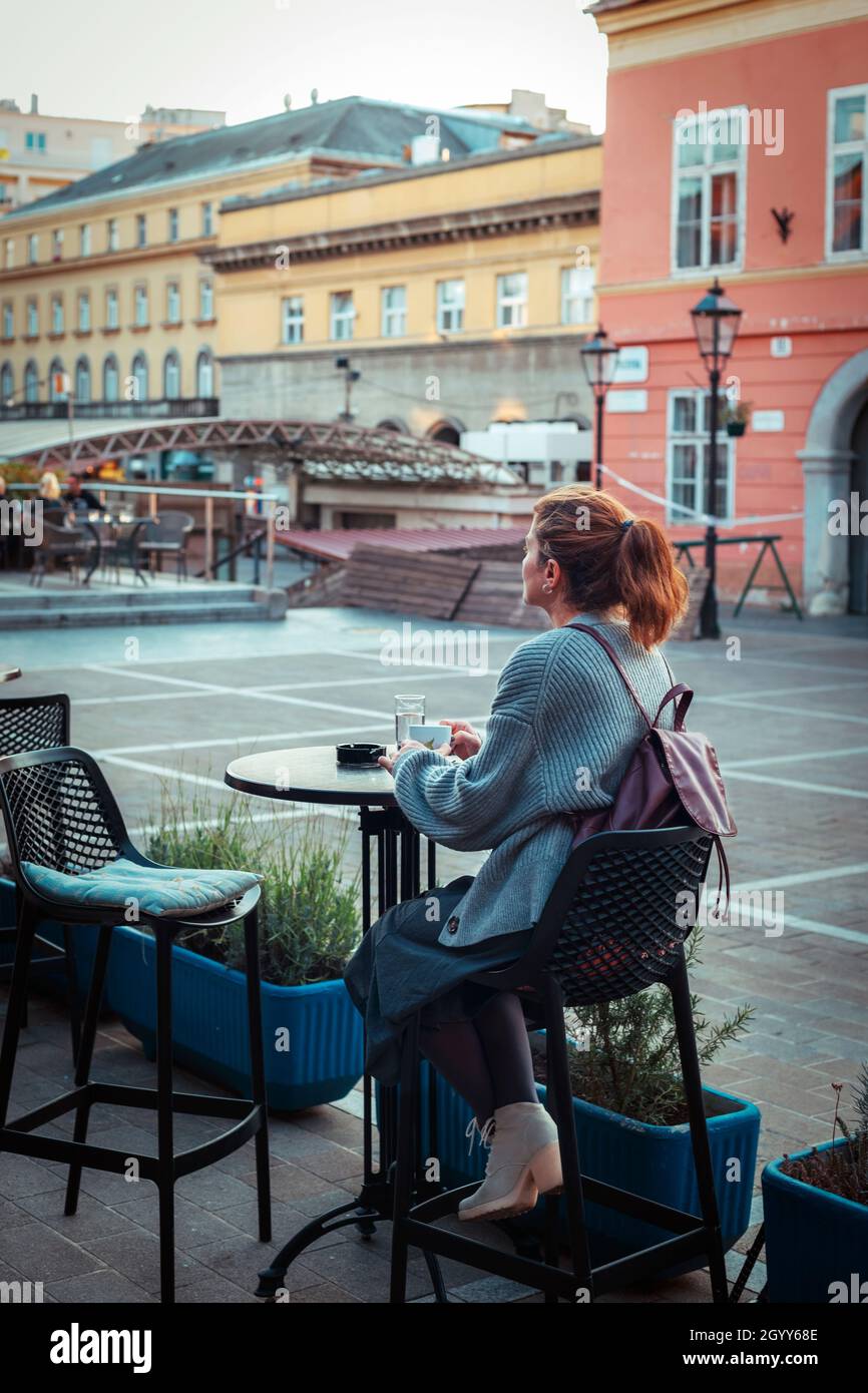 Ragazza che beve caffè a un tavolo in un caffè di strada. Foto Stock