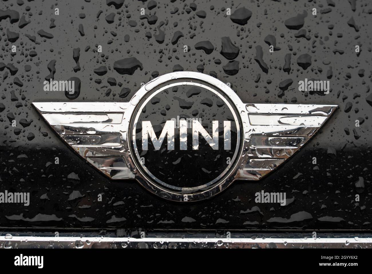 Un logo e un distintivo color argento per il marchio Mini su un cofano nero coperto da gocce d'aria di una mini berlina, Regno Unito Foto Stock