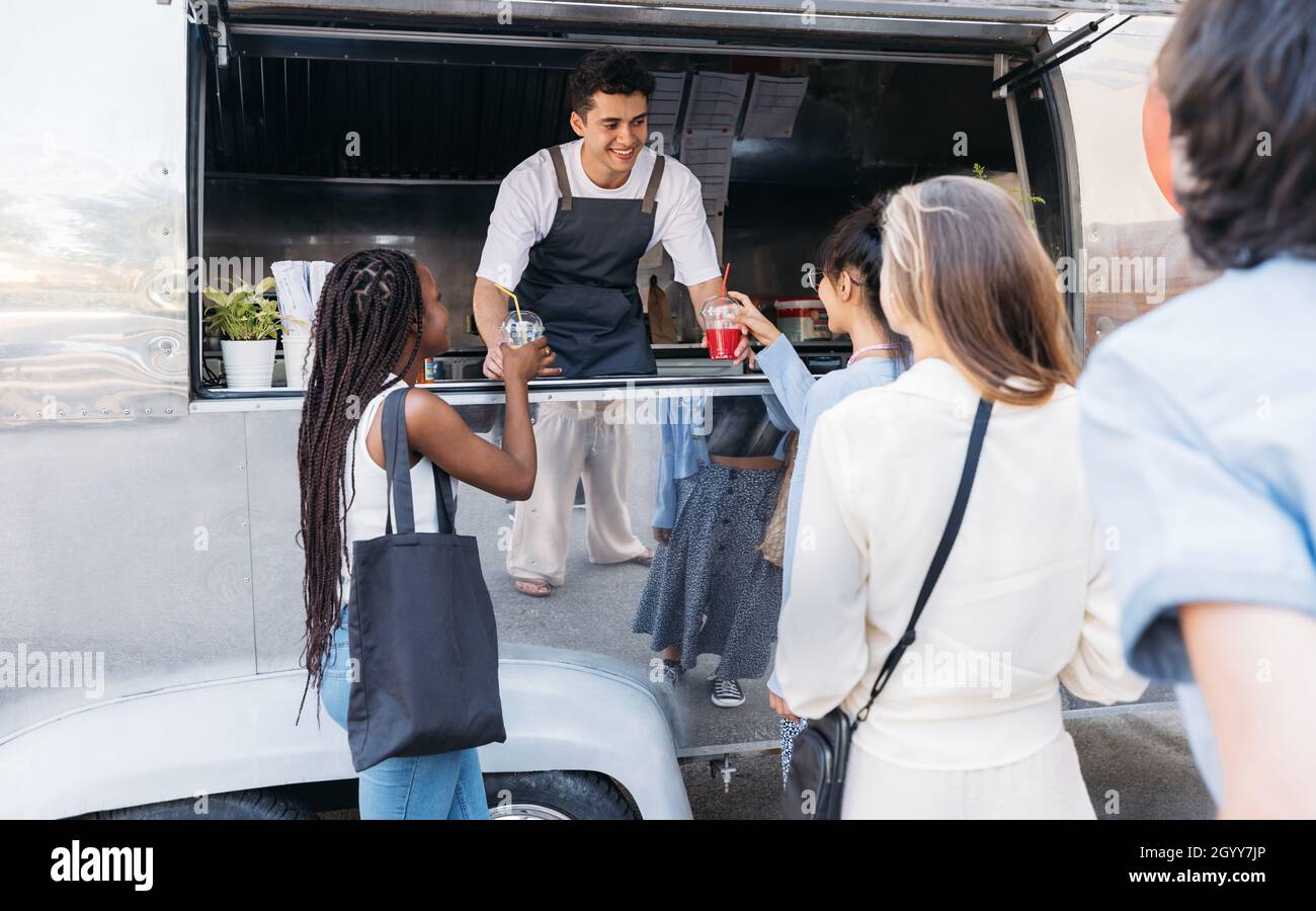 Coda di persone al camion alimentare. Un venditore sorridente offre bevande ai clienti. Foto Stock