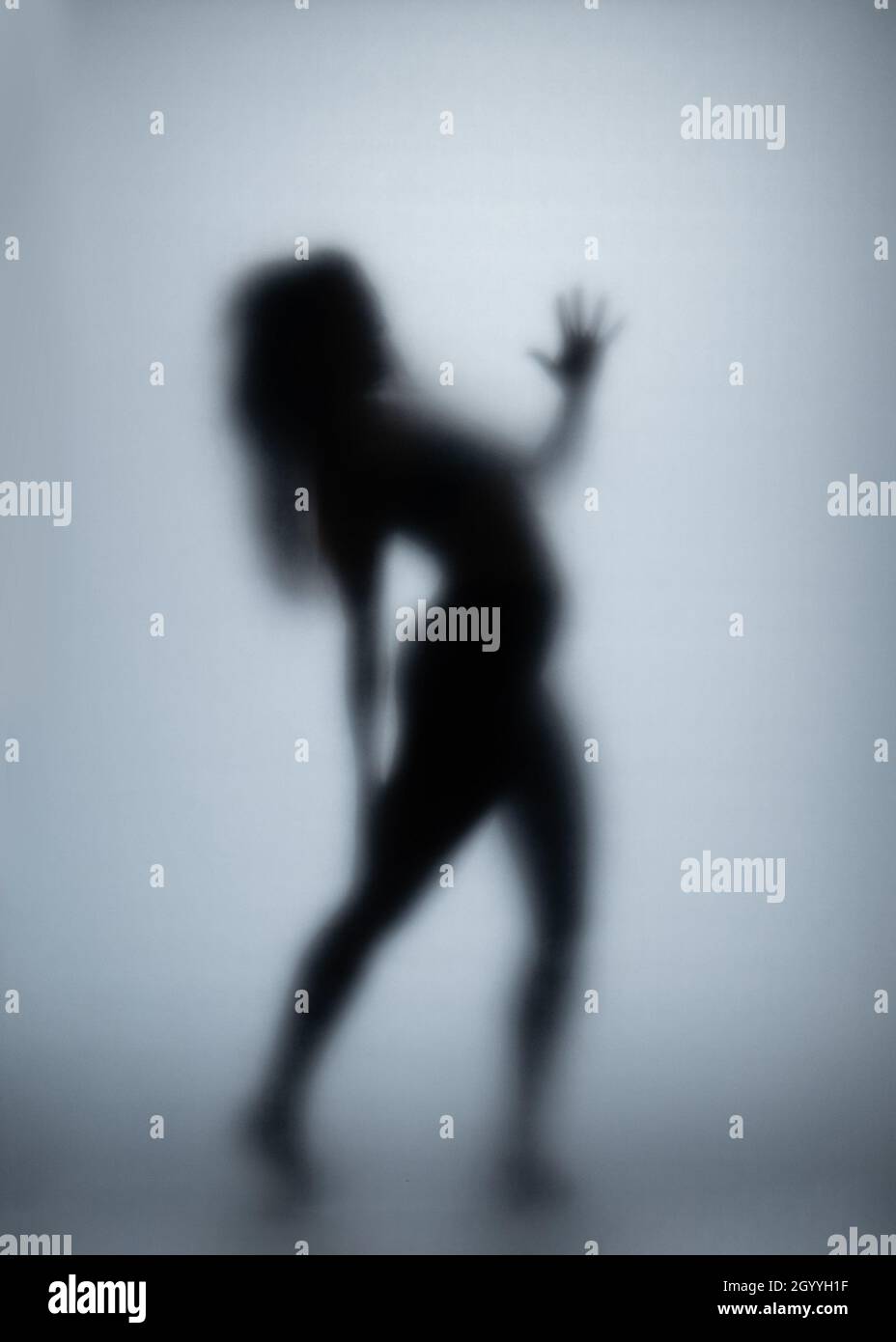 Donna posseduta gratta vetro con le mani, la silhouette femminile creepy, orrore. Spaventosa creatura spettrale dietro il vetro. Foto Stock