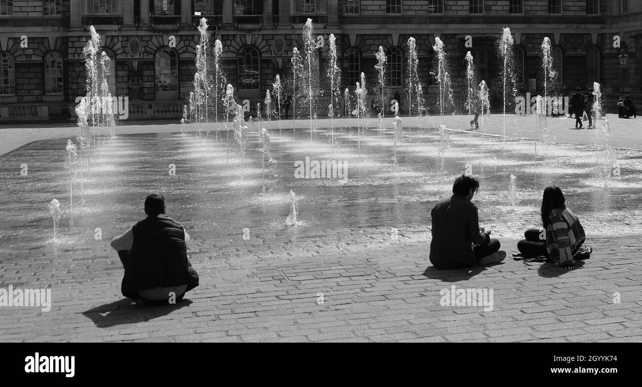 Al sole di primavera, le persone si siedono e si godono le fontane d'acqua nel cortile della Somerset House, Londra Foto Stock