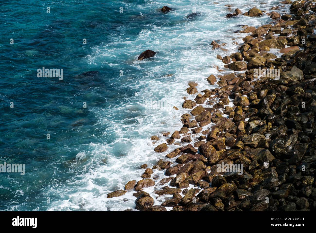 le onde dell'oceano colpiscono la spiaggia di pietra nera, il paesaggio roccioso della costa Foto Stock