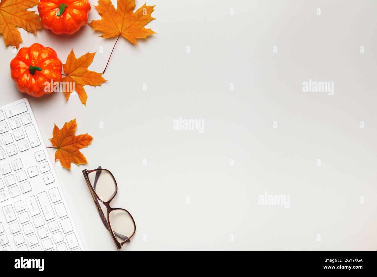 Vista dall'alto di un desktop bianco con tastiera, occhiali, foglie d'autunno con zucche. Spazio per la copia di Flat Lay Foto Stock