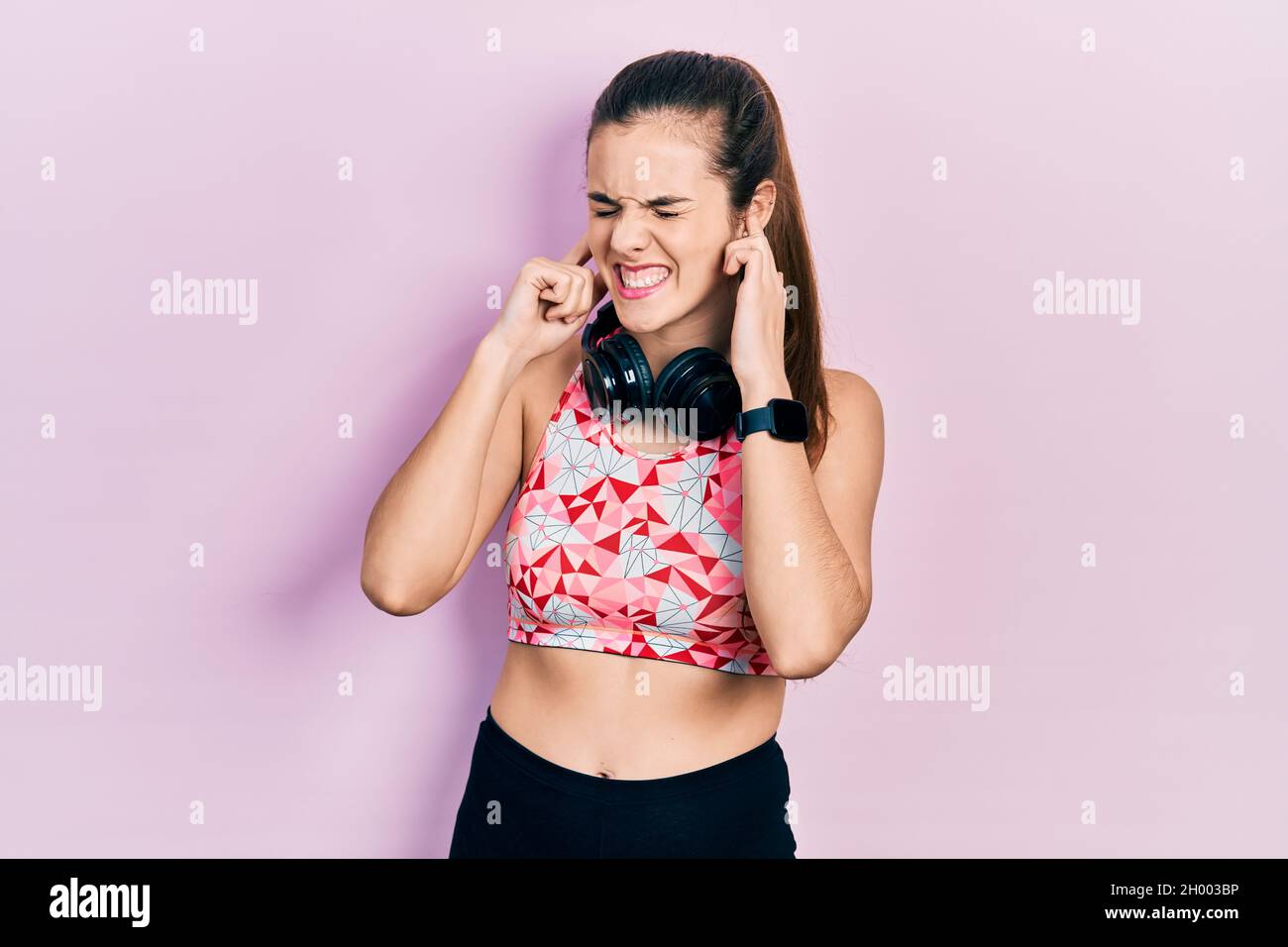 Giovane adolescente bruna indossa abiti da palestra e cuffie che coprono le  orecchie con le dita con un'espressione infastidita per il rumore della  musica ad alto volume. Sordo Foto stock - Alamy