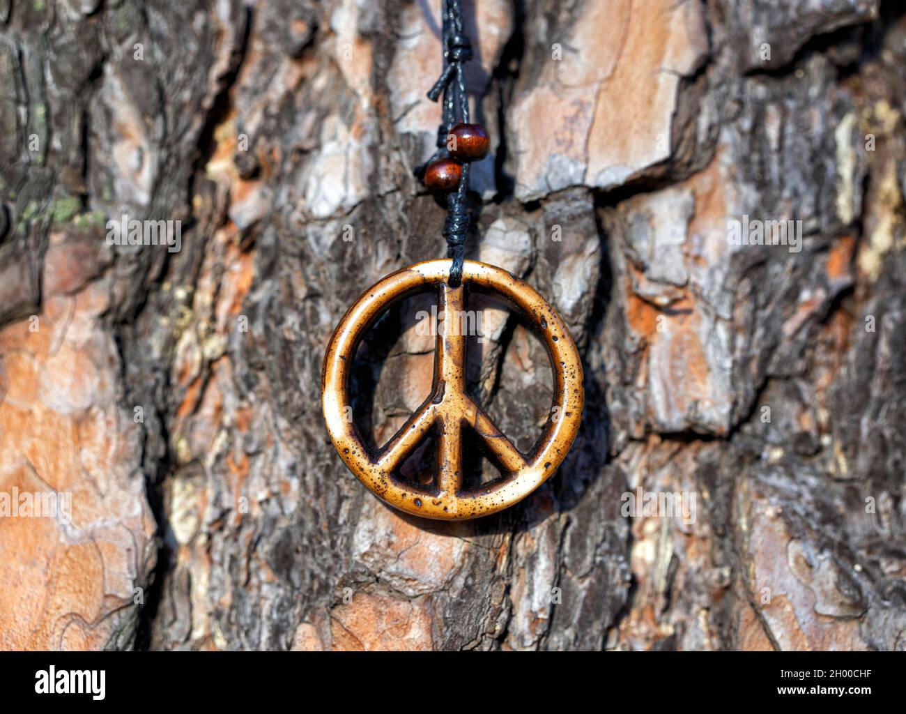 Primo piano di una collana di legno segno di pace contro una corteccia di tronco di albero, fuoco selettivo Foto Stock