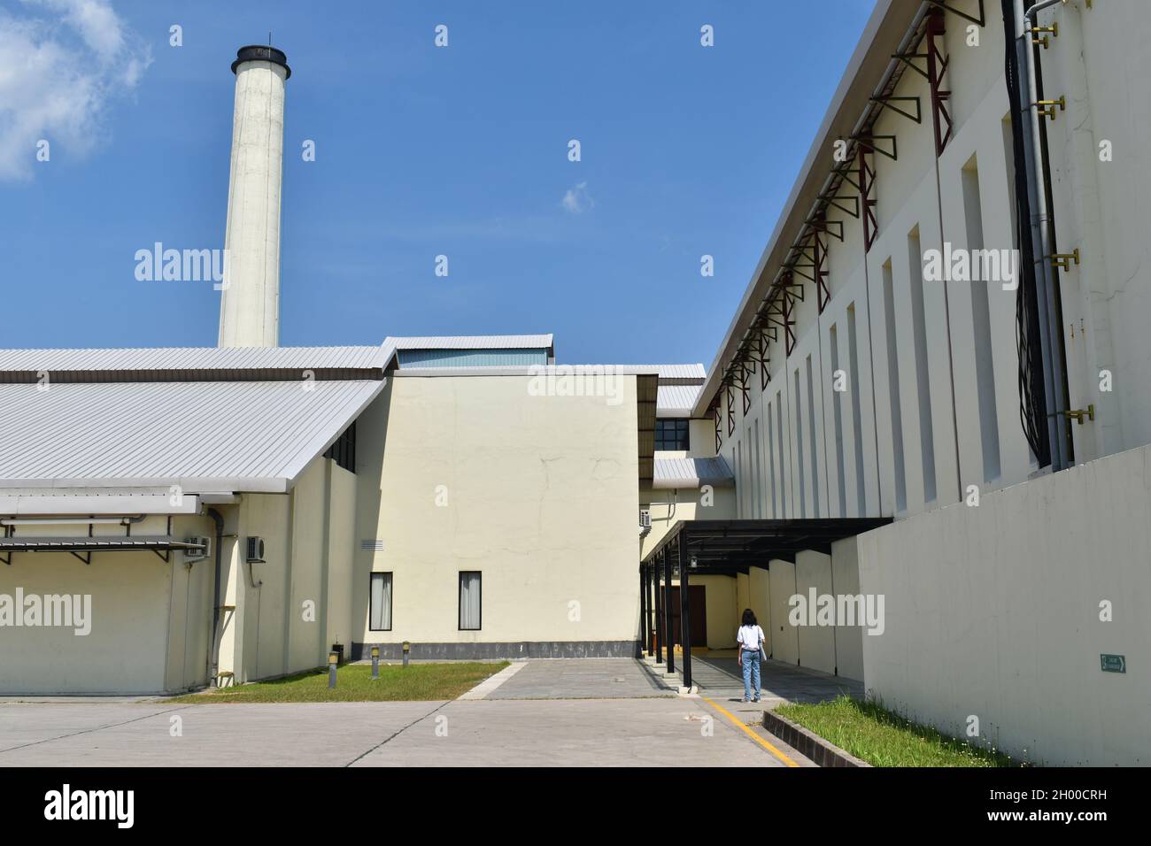 Una ragazza che si trova all'esterno di un edificio spazioso con camino nell'altro lato. De Tjolomadoe, centro culturale ed espositivo. Surakarta, Indonesia. Foto Stock