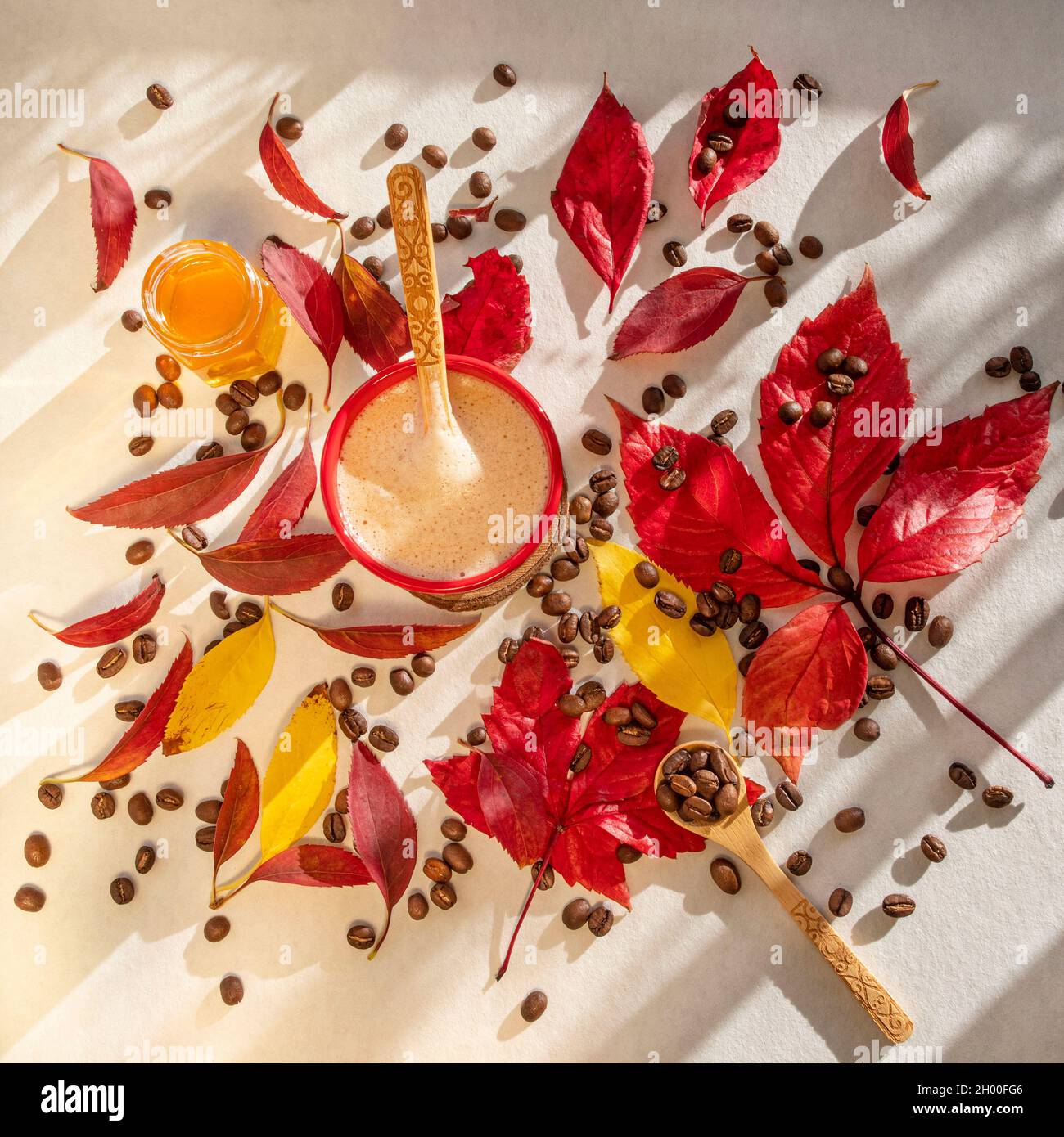 Tazza di caffè caldo in chicchi di caffè torrefatto e foglie d'autunno rosse e gialle su un tavolo Foto Stock