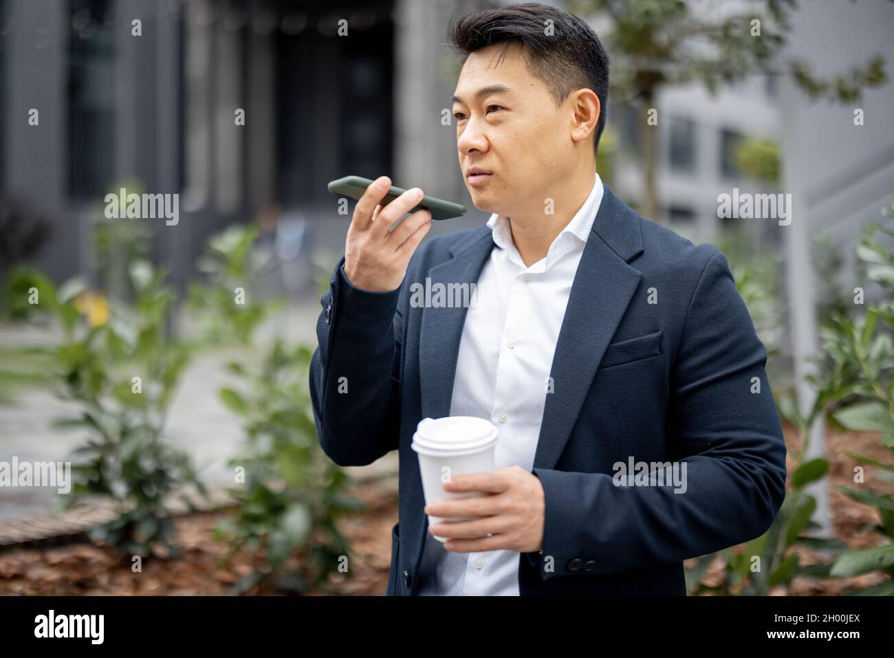 Uomo d'affari con una tazza di caffè che chiama sullo smartphone Foto Stock