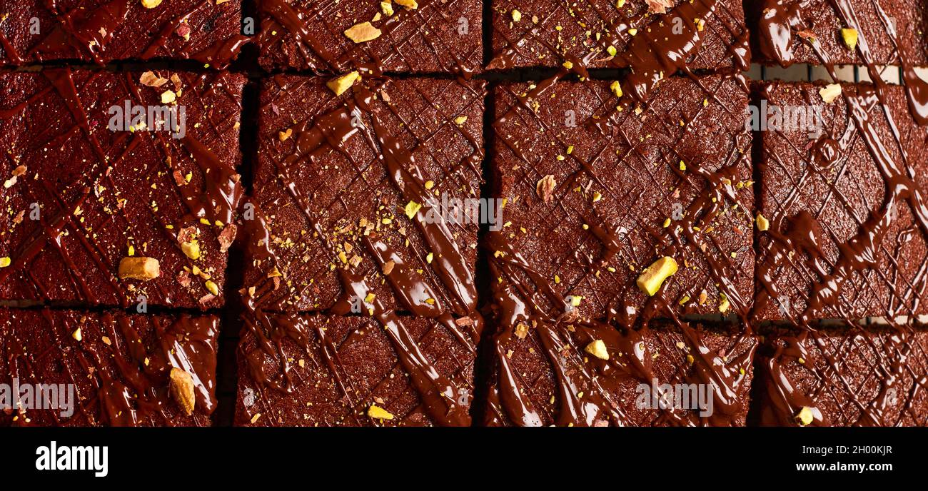 Quadrati di cioccolato con pistacchio e fragole su un supporto metallico su uno sfondo di pietra chiaro, vista dall'alto, composizione orizzontale. Disposizione piatta. Foto Stock