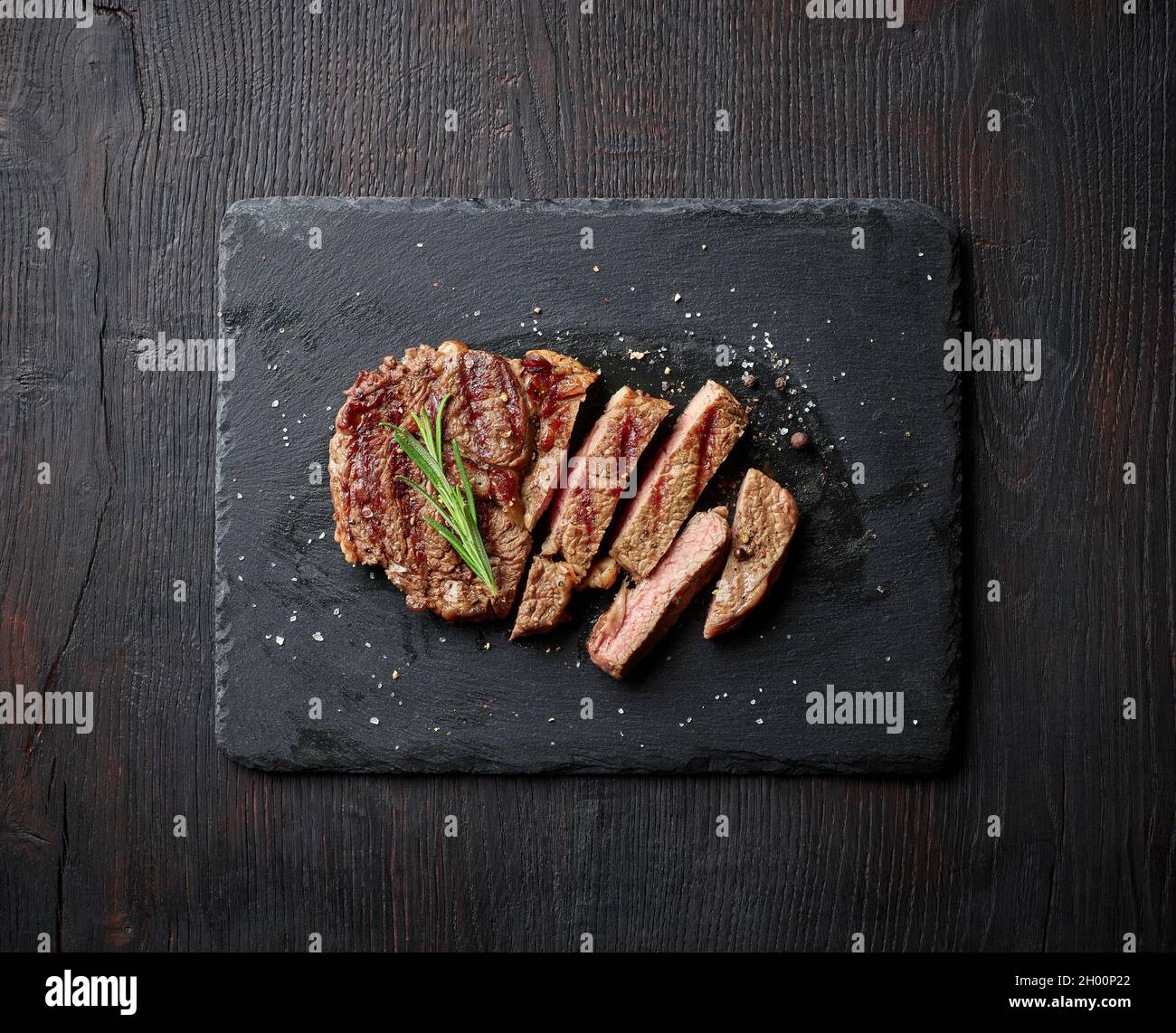 Bistecca di entrecote e rosmarino grigliati a fette su tavola di pietra nera, vista dall'alto Foto Stock