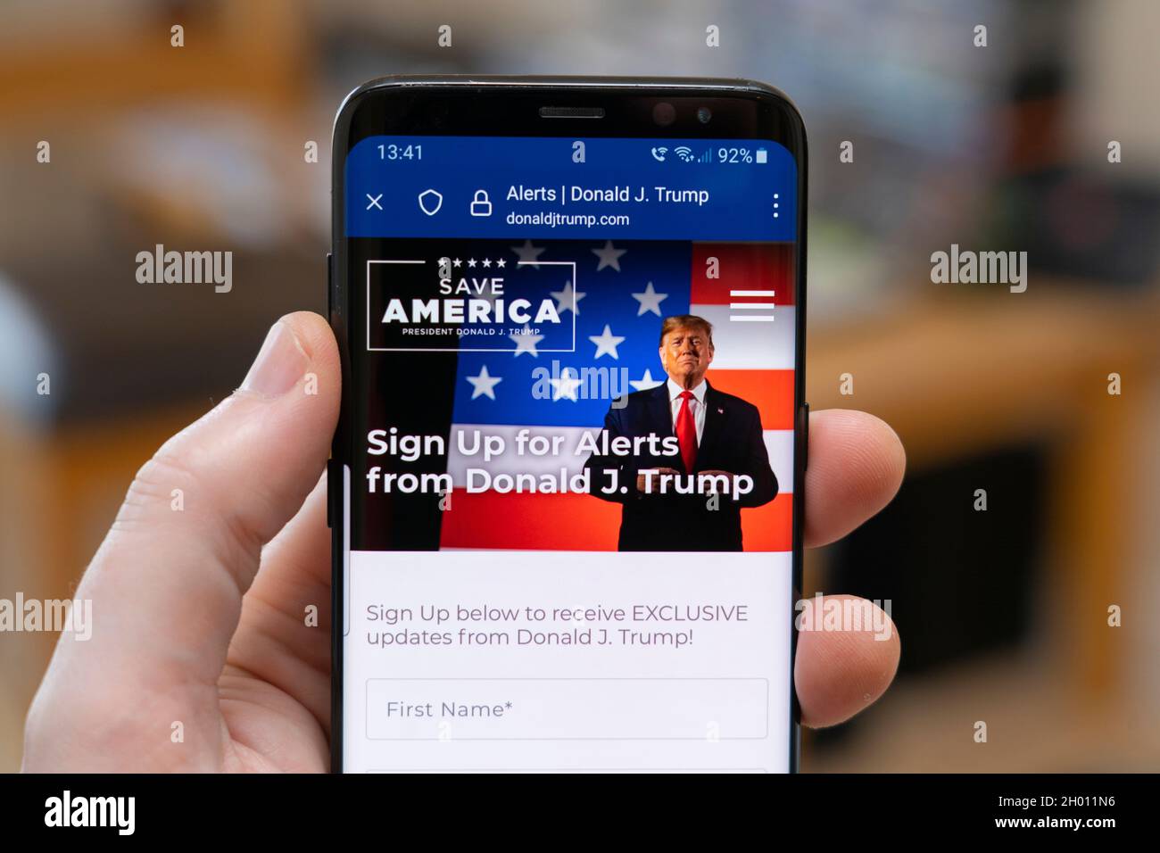 Mano dell'uomo che tiene uno smartphone che mostra il sito web di Donald J. Trump di breve durata che ora si reindirizza a una pagina di riempimento chiedendo agli utenti di iscriversi per gli avvisi Foto Stock