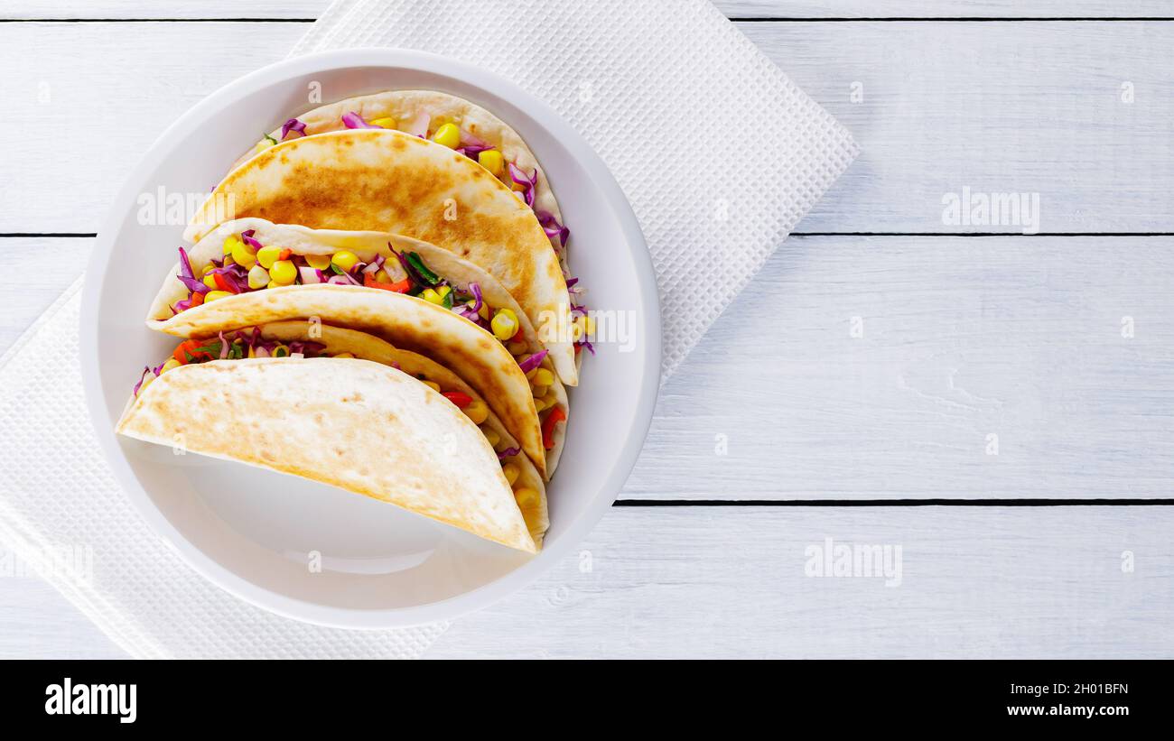 Tacos vegani con mais, cavolo viola e pomodori su un piatto bianco. Tacos messicani con verdure diverse su tavole bianche. Cibo sano. Cubici messicani Foto Stock