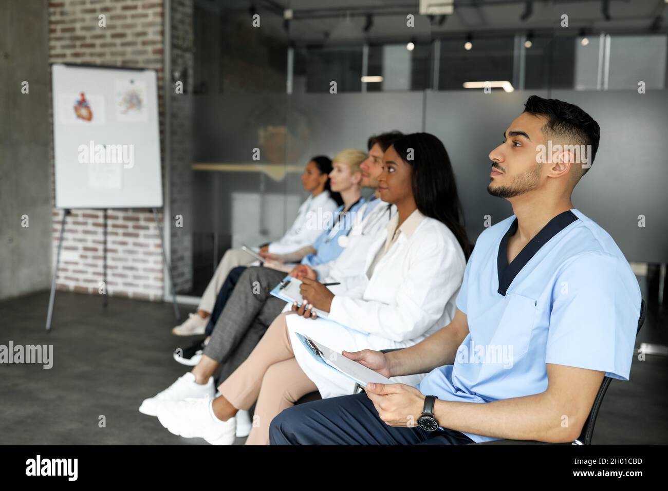 Il gruppo multirazziale di medici ha concentrato uomini e donne in abbigliamento da lavoro frequentando una conferenza medica in clinica, seduto in fila e guardando lo spazio per le copie Foto Stock