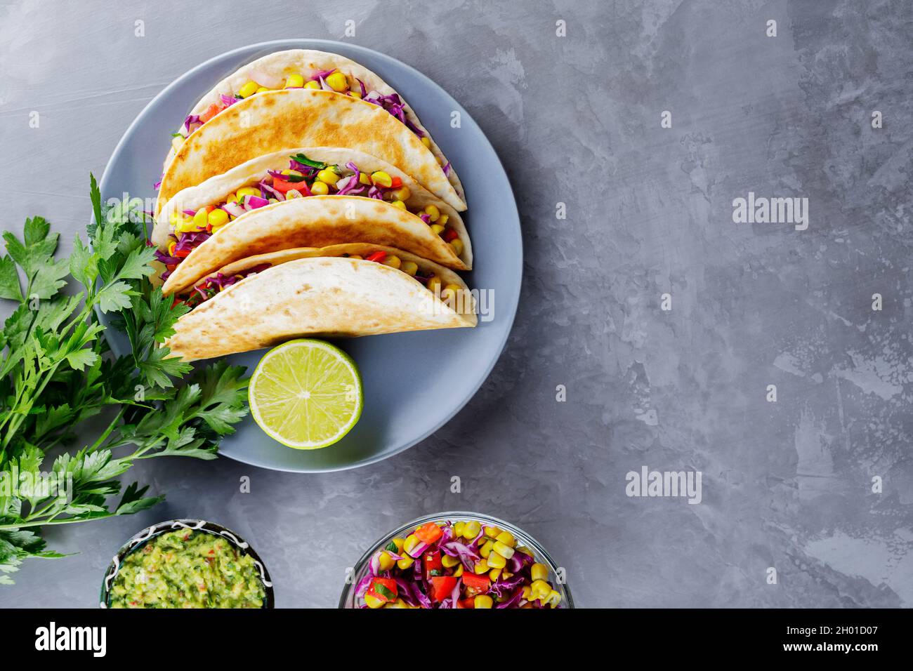 Tacos messicani con verdure e guacamole su sfondo grigio. Tacos vegani con mais, cavolo viola e pomodori su un piatto grigio. Spazio di copia. Top vi Foto Stock