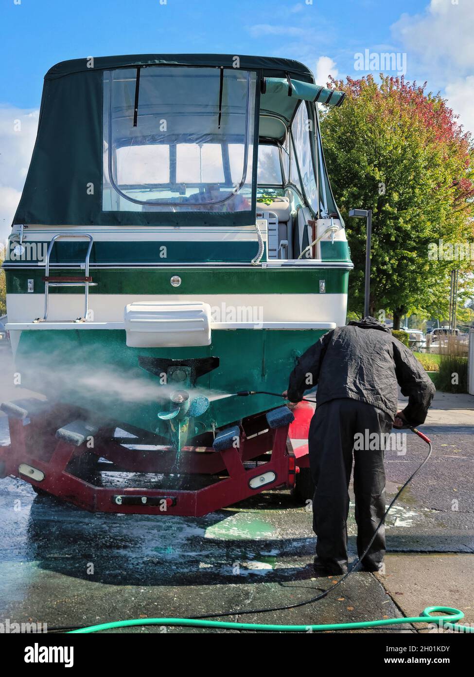 Uomo caucasico che indossa un vestito nero impermeabile mentre a pressione lavaggio barcha a motore Foto Stock