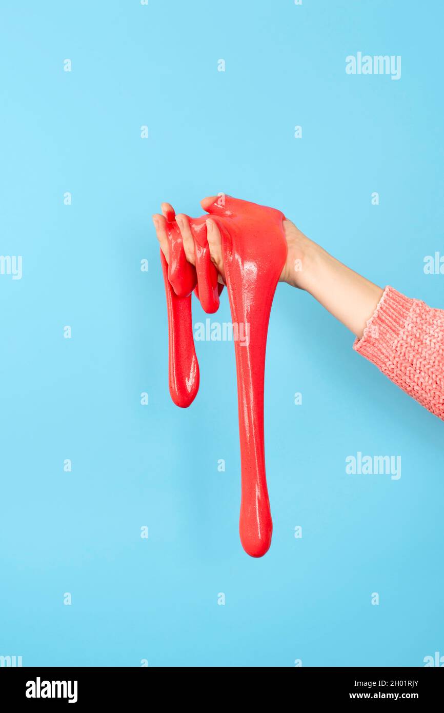 Primo piano su rosso lucido o corallo slime nella mano isolato su sfondo blu. Concetto di divertimento e di stress. Foto Stock