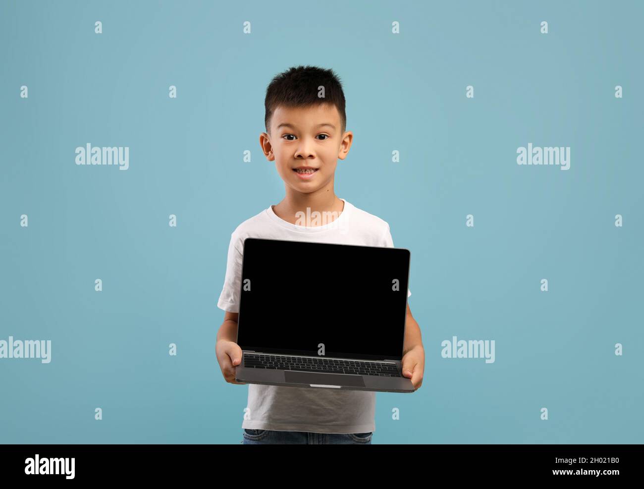Little Asian Boy dimostrando notebook con schermo nero vuoto, cheerful coreano maschio bambino raccomandare sito web per l'istruzione online, mostrando copia gratuita Foto Stock