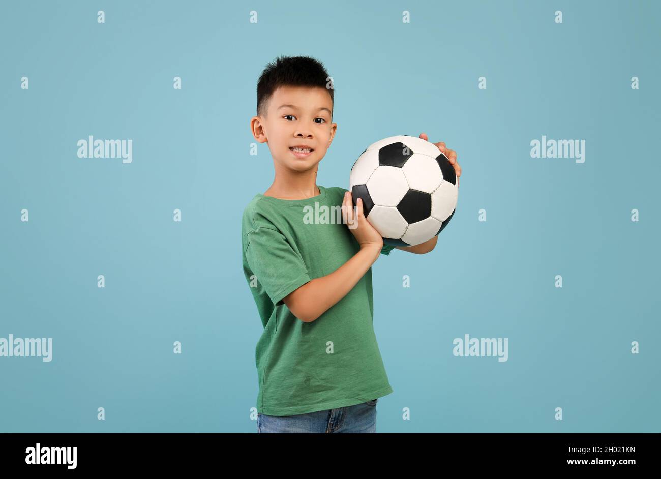 Sportsman piccolo. Eccitato ragazzo asiatico in posa con pallone da calcio in mani su sfondo blu in studio, carino Premeen coreano maschio Kid guardando fotocamera, Foto Stock