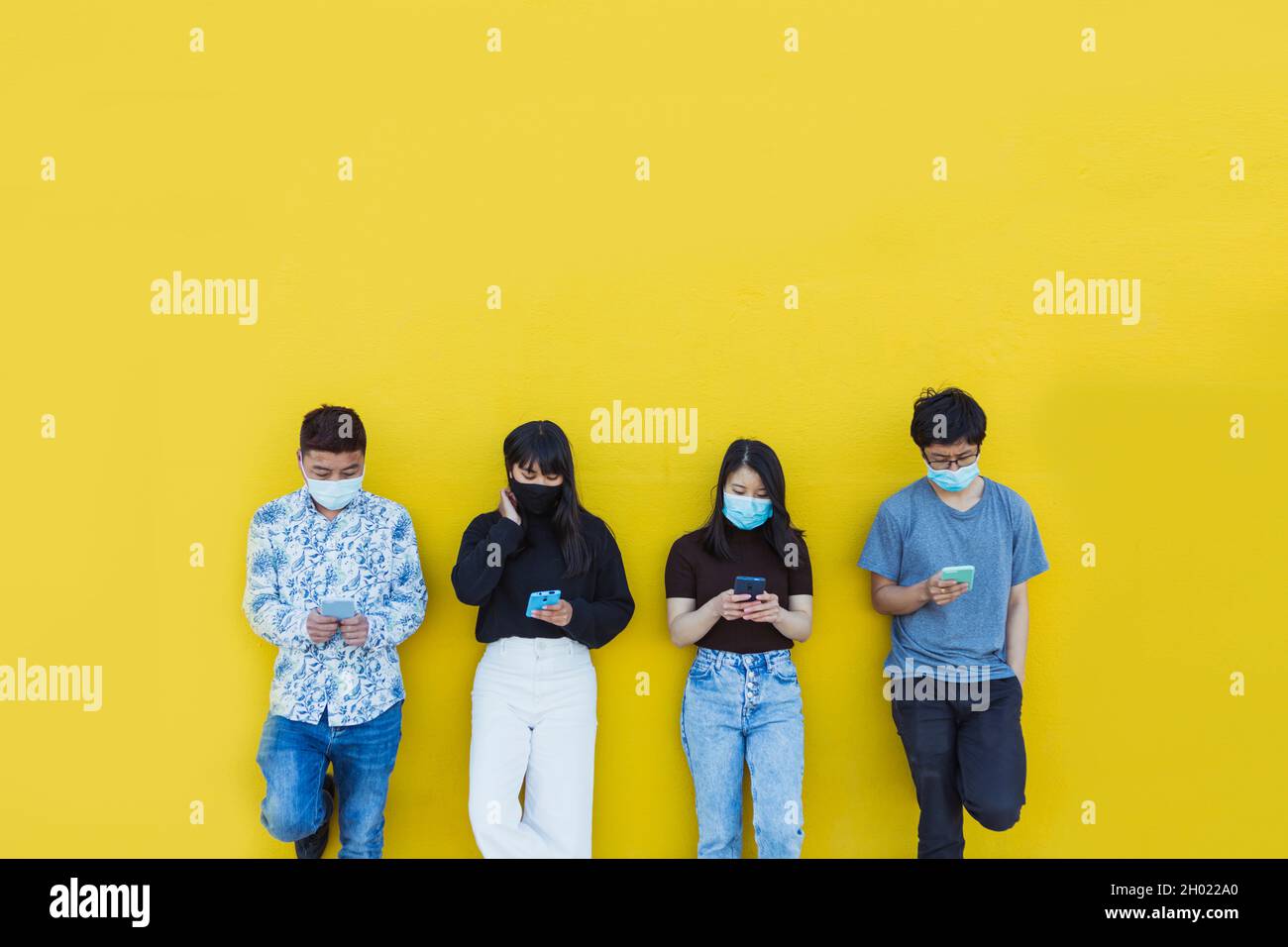 Amici asiatici in maschera protettiva viso utilizzando smartphone all'aperto Foto Stock