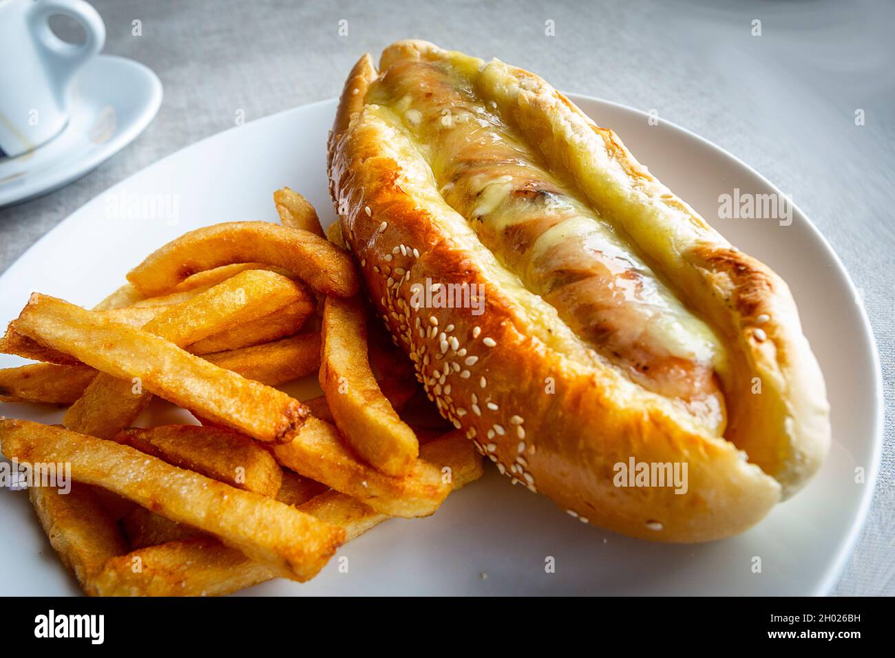Un hot dog al formaggio in pancia su un piatto con patatine fritte. Foto Stock