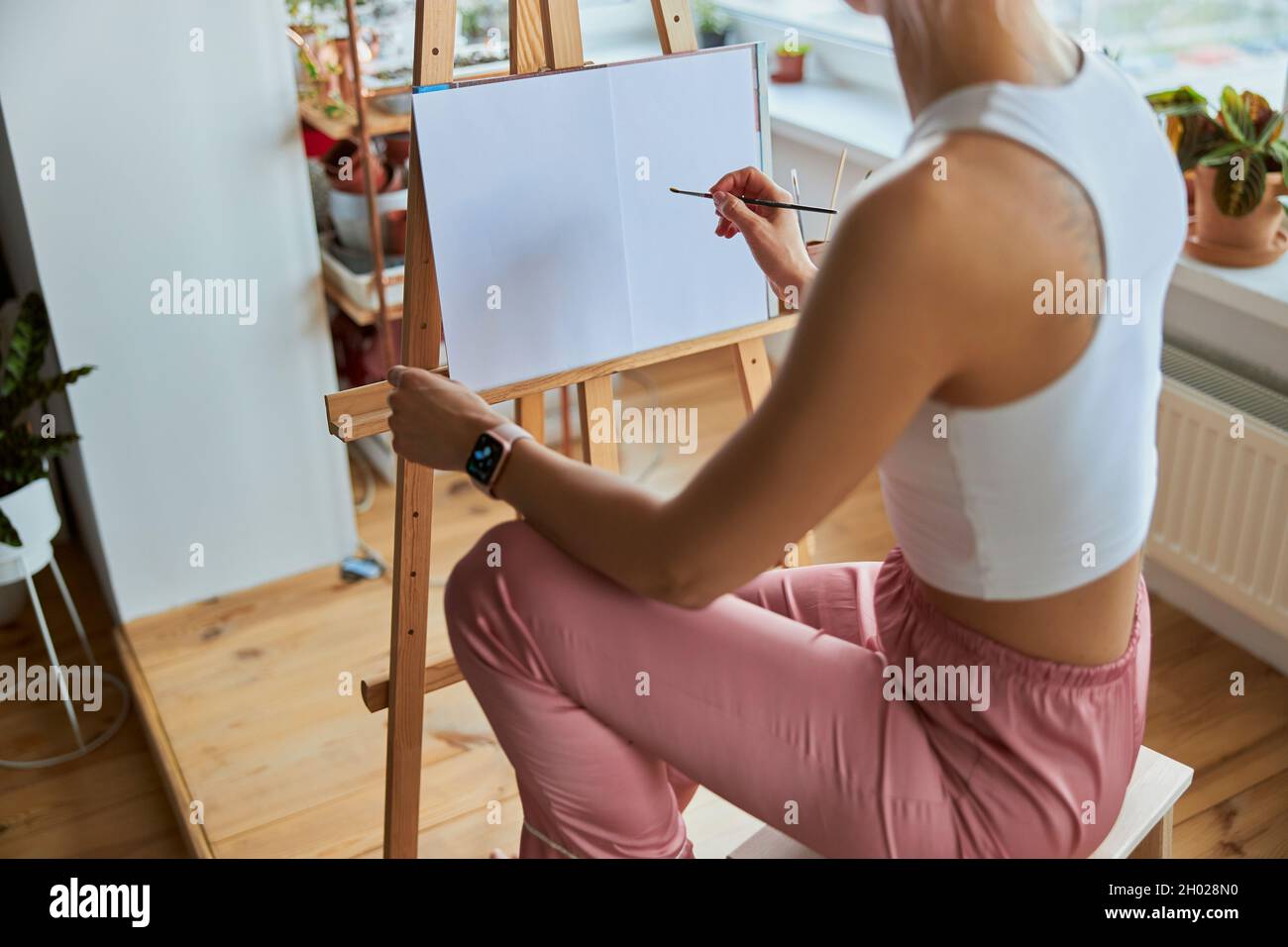 La giovane donna disegna la foto su tela con spazzola a cavalletto in legno sul balcone Foto Stock
