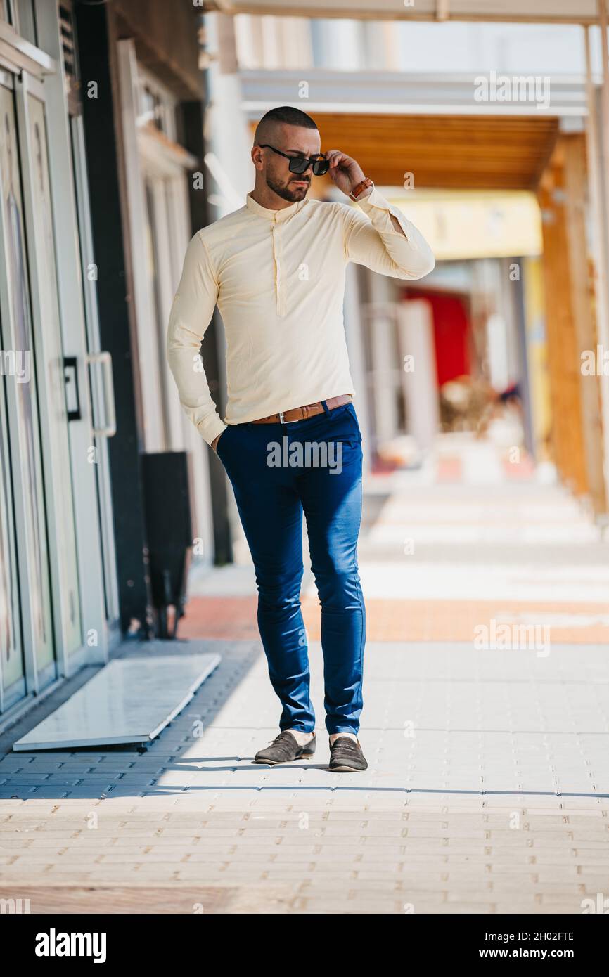 Bell'uomo caucasico che indossa una camicia gialla e occhiali da sole in posa all'aperto Foto Stock