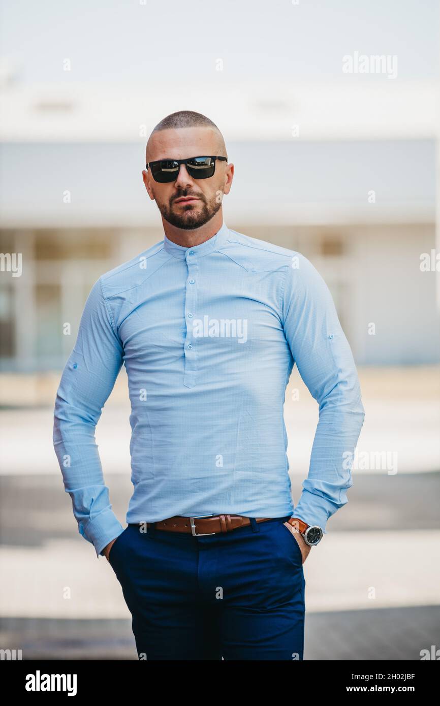 Bell'uomo caucasico che indossa un'elegante camicia blu chiaro e occhiali  da sole in posa all'aperto Foto stock - Alamy
