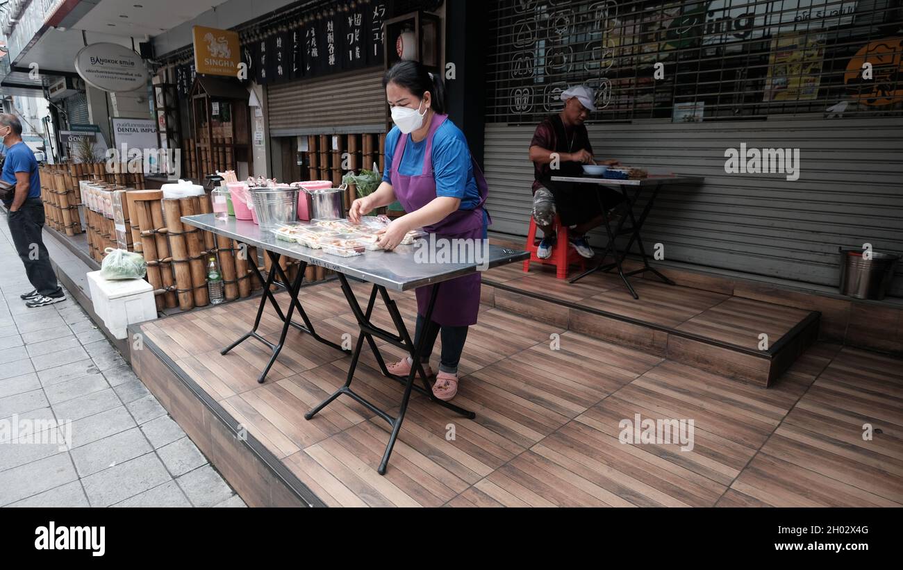 Lady Setting Display e uomo seduto mangiare cibo di strada al tavolo su Asoke Road Sukhumvit Soi 21 Bangkok Thailandia Foto Stock