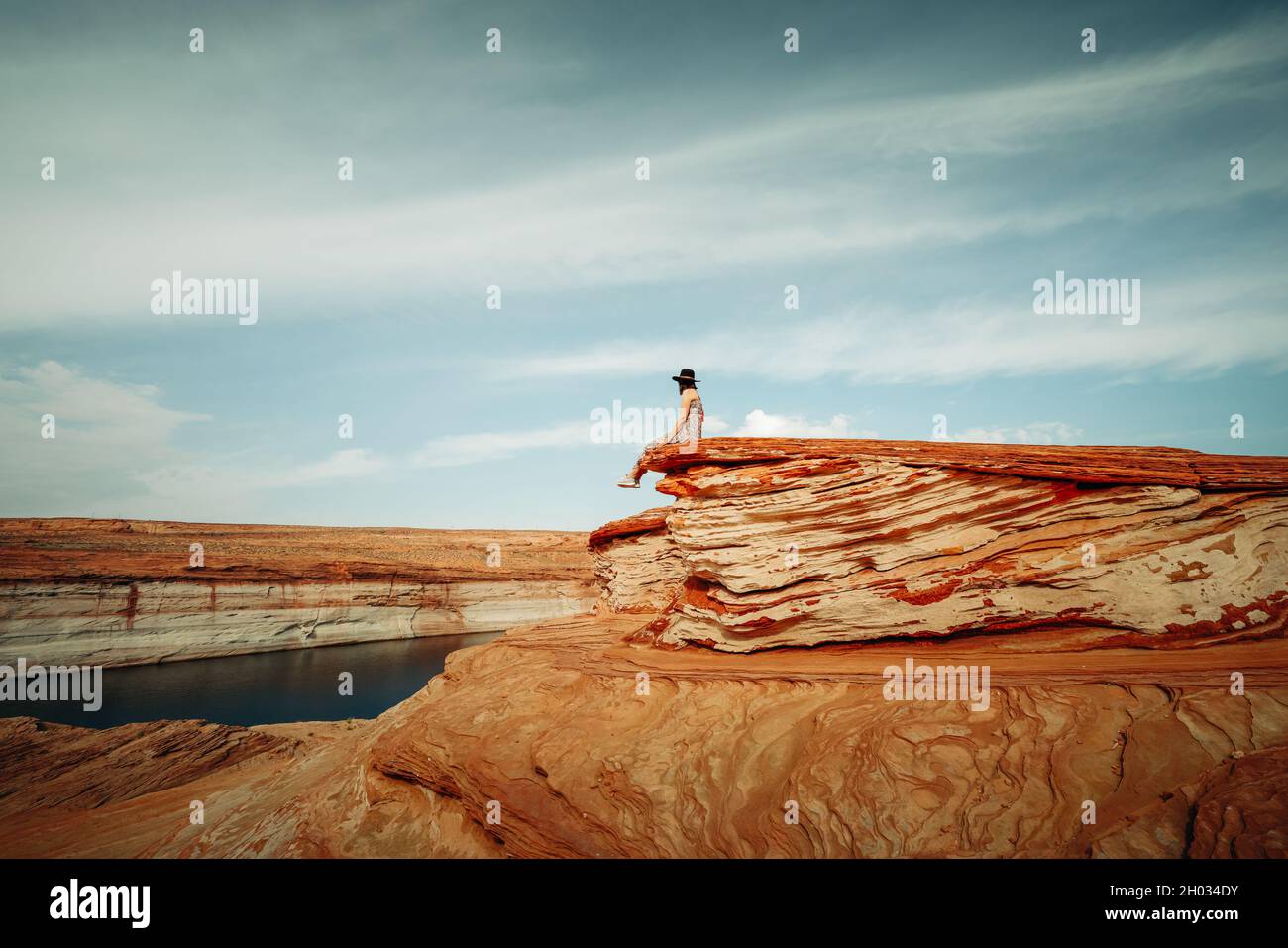Donna seduta su una scogliera. Scogliere di arenaria, lago Powell e cielo nuvoloso sfondo. Esplorando le catene, Glen Canyon, Page, Arizona Foto Stock
