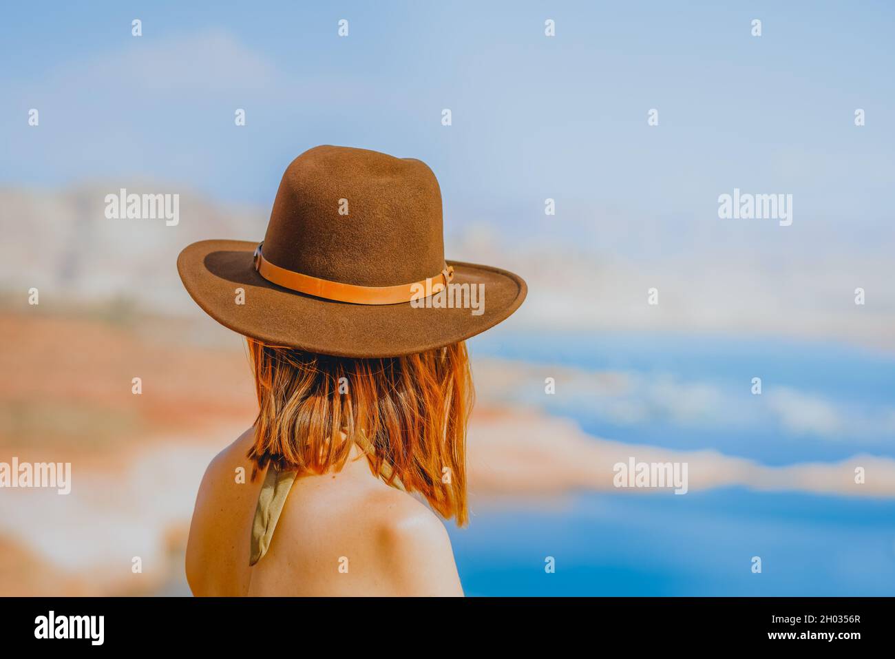 Donna dai capelli rossi che indossa un cappello sulla spiaggia che si affaccia sul lago, vista posteriore Foto Stock