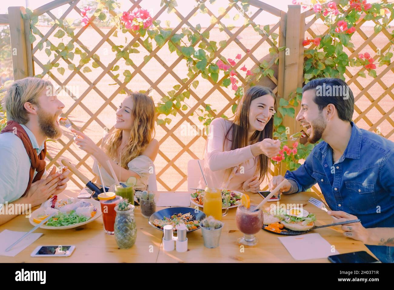 Belle coppie giovani si nutrono a vicenda e sorridono mentre mangiano cibo vegano in terrazza a casa. Concetto di cibo e amore. Foto Stock