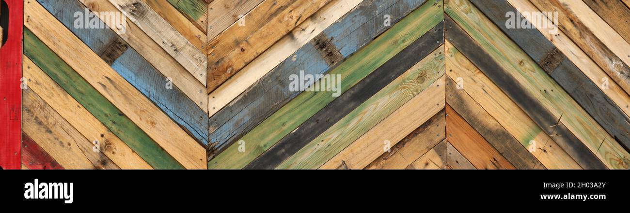 Motivi geometrici astratti altamente unici realizzati con palette di legno tagliate riciclate disposte a strisce diagonali. Tavole a ciclo superiore multicolore Foto Stock